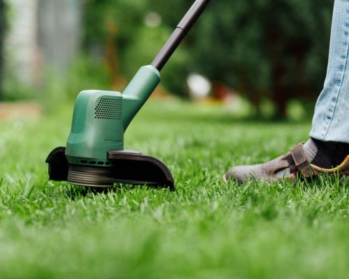 Man mows tall grass with an electric trimmer. Yard care concept Man mows tall grass with an electric trimmer. Yard care concept